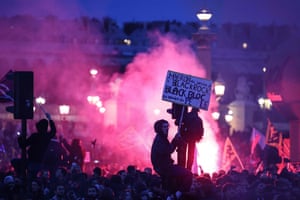 A protester on a traffic light holds a placard reading ‘Macron at the service of Black Rock, Black bloc at the service of the people’ in Paris