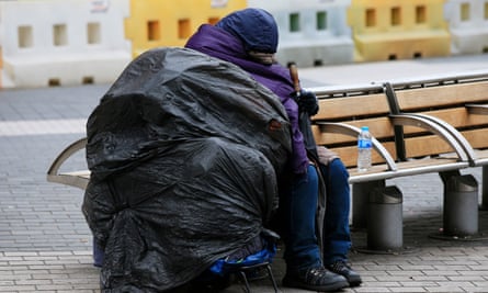 A homeless person sleeps on a bench on a London street<br>