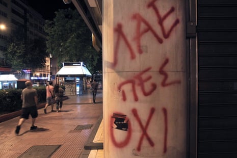 People walk by a graffiti reading ‘People say NO’ on the wall of a closed bank in Athens tonight.
