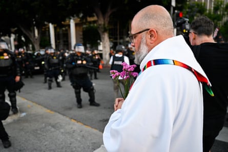 A priest holds flowers as armed riot police stand nearby
