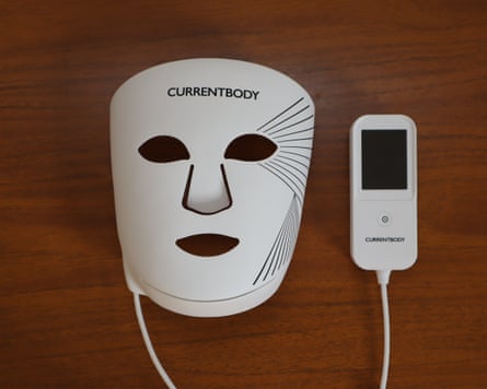 A white CurrentBody LED face mask and its controller sit on a wooden surface