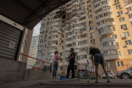 People clean debris in front of a residential building damaged during a Russian air strike in Kyiv.