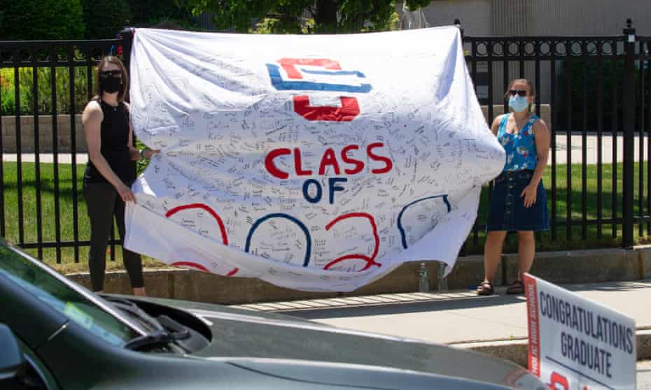Teachers stand with a large banner with the names of the graduating seniors of the class of 2020 while cars carrying the graduates drive past outside Central Catholic high school in Lawrence, Massachusetts.