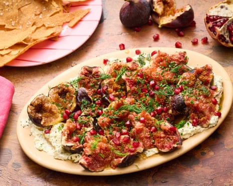 A platter of labneh, figs, pomegranate and herbs on a wooden table.