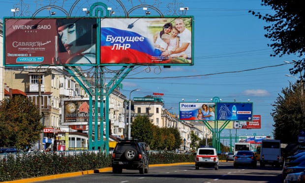 Vehicles drive past advertising boards, including panels displaying pro-Russian slogans, in a street in Luhansk
