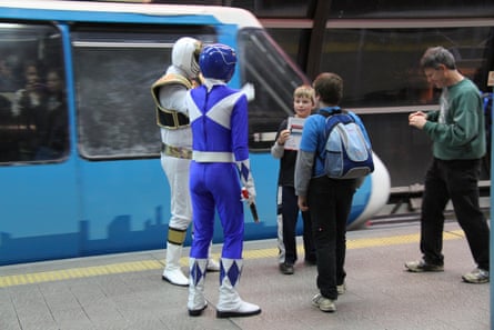 Two people dressed up as Power Rangers speak to travellers on a monorail station.
