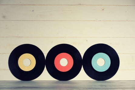 Three blank vinyl records, with centres coloured yellow, red and blue, on a wooden background