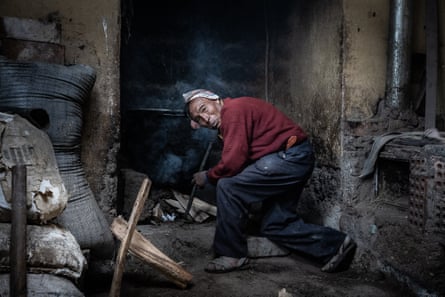 A man from the Chahuaytire community, bent over the fire in his kitchen, prepares soup for his family
