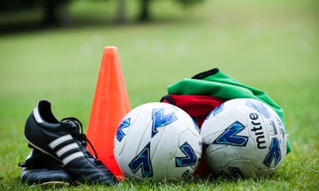 Football boots, a red cone, two footballs and green and red tops on the grass 