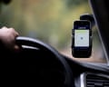 A hand on a steering wheel with the Uber app opened on a phone attached to the windshield