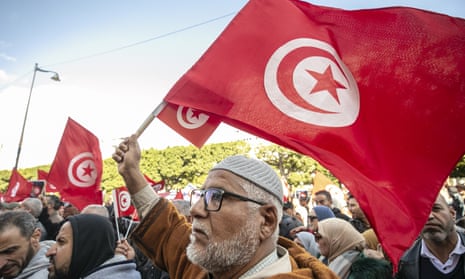 An older man in a skull cap waves a Tunisian flag