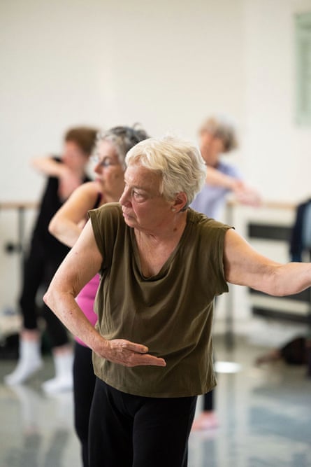 A lady with white hair and a brown top holds a dance position during a class for over 60s