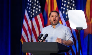 man talks at podium in front of american flags