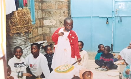 A young African girl smiles at the camera as she cuts a birthday cake. Other children are sitting around her