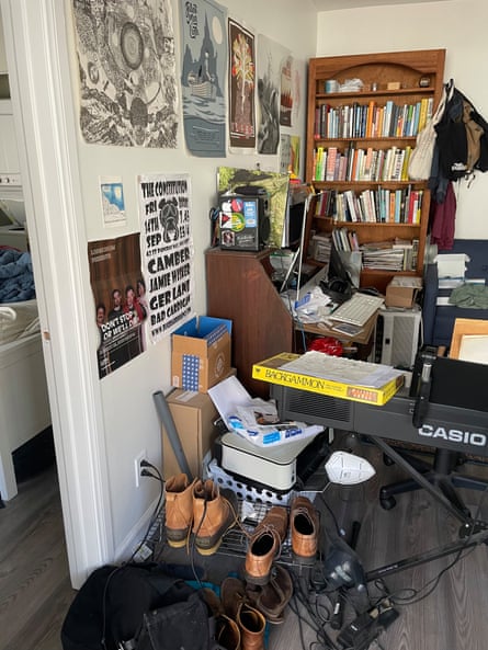 messy room with a casio keyboard, an old writing desk, lots of shoes and boots on the floor, posters all over the wall,  a backgammon board on the keyboard with a drawing on top of it