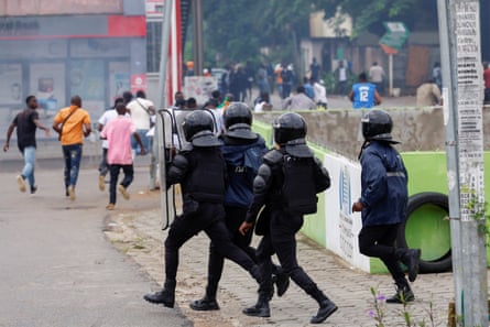 Riot police run after protesters who are fleeing along a road in the city