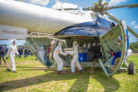 Men in white hazmat suits unloading boxes from a cargo helicopter
