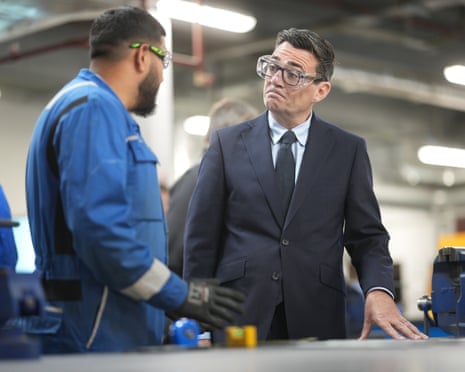 Andy Burnham wears goggles as he talks to a man in an industrial setting.