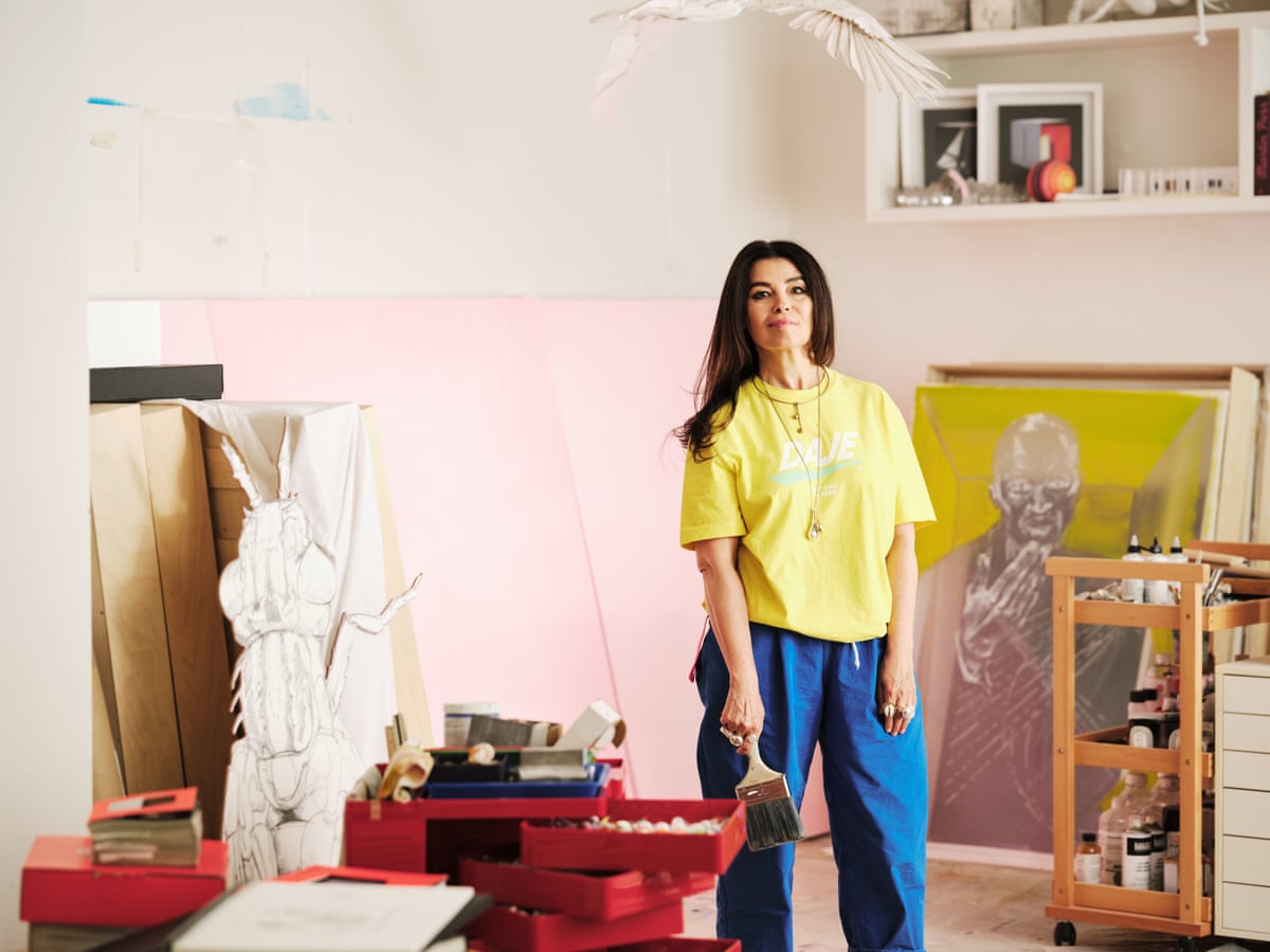 Es Devlin in a yellow T-shirt and blue trousers standing in her studio.