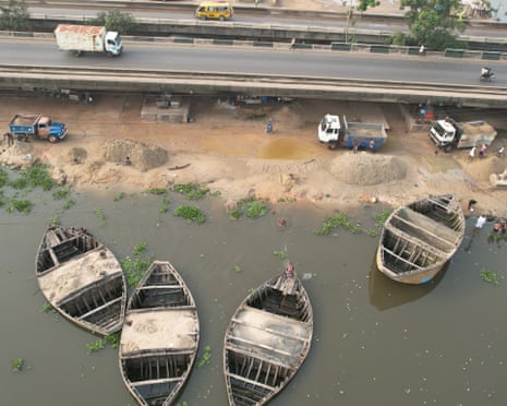 ‘The water is no longer our friend’: how dredging is pushing Lagos Lagoon towards ecosystem collapse – photo essay Four wooden boats in the water next to a motorway.