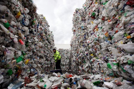 A worker sweeps stacks of plastic bottles at a recycling plant in Dagenham, Essex, UK.