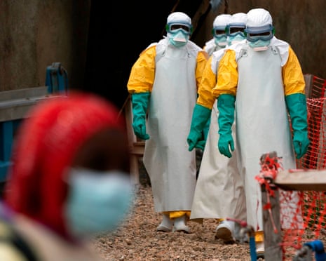 Health workers in protective gear walk toward the camera at an Ebola treatment centre