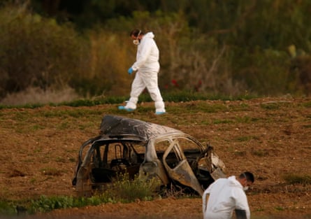 Two forensic officers in white boiler suits near a totally burnt-out car.