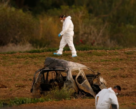 Two men in white forensics suit either side of a burnt-out car in the middle of a field