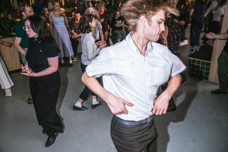 A man in a white shirt and dark trousers twirls enthusiastically on the dancefloor