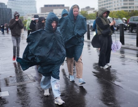 People wearing hooded rain ponchos walk along wet Westminster Bridge in blustery weather
