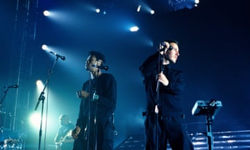 Two men on stage dressed in black under bright lights