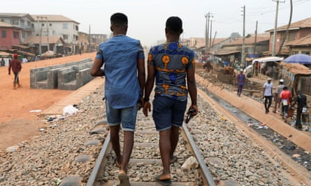 Two Nigerian men seen from behind walking beside each other along a railway track 