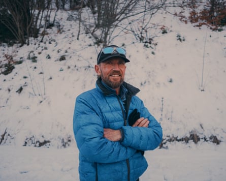 A man in a blue padded jacket stands in front of a snowy bank.