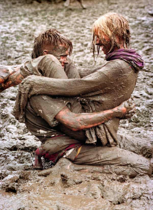 A young woman and young man, both completely muddy from head to toe, embrace