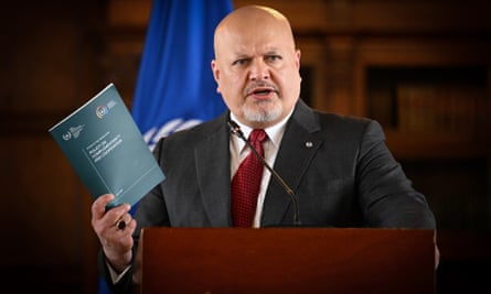 Karim Khan standing at a lectern holding a book titled Policy on Complementarity and Cooperation