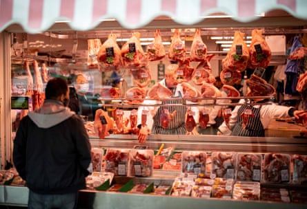 a man with his back to the camera stands admiring a window full of meat in a butchers shop