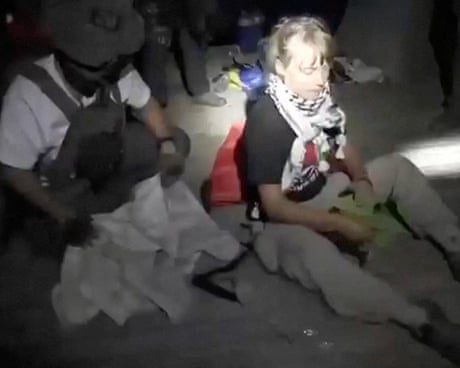 Greta Thunberg sitting next to a person wearing military gear in the dark