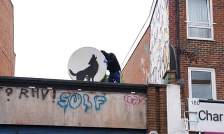 A man in a balaclava removing a satellite dish with a wolf spraypainted on it