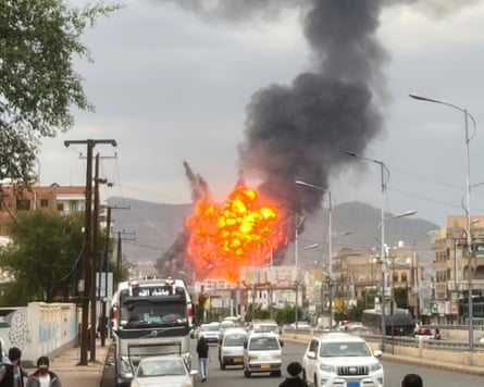 Flames and smoke rise in the distance with a main road in the foreground.