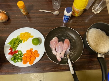 A plate with vegetables arranged next to a small pan with pieces of chicken and another pan with rice on a dark wooden surface.