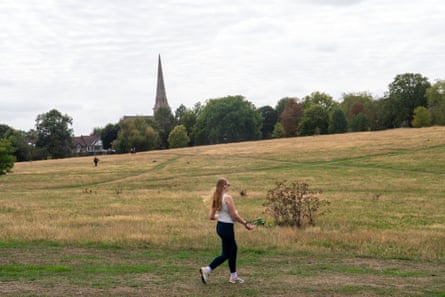 A jogger runs through partially re-greened grassland with trees and a church in the background
