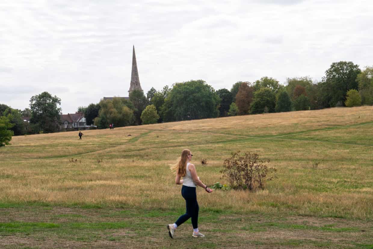 A jogger runs through partially re-greened grassland with trees and a church in the background