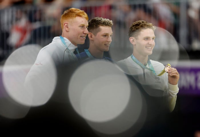 Gold Medallist Scotland’s Duncan Scott celebrates on the podium alongside silver medallist England’s Tom Dean and bronze medallist New Zealand’s Lewis Clareburt.