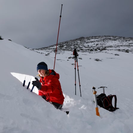 Sam Noble kneeling in her snow pit, surrounded by pieces of survey equipment