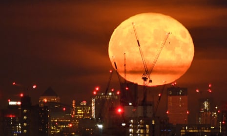 A full moon rises behind skyscrapers at UK’s banking headquarters at Canary Wharf in east London.
