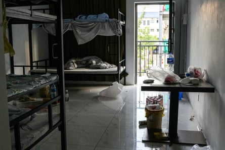 Water and drinks bottles and bags of food are left on the floor and on a small table in a room containing multiple bunk beds.