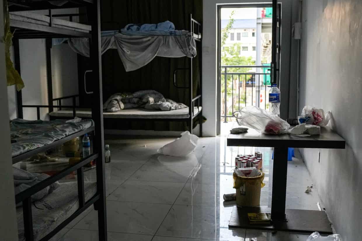 Water and drinks bottles and bags of food are left on the floor and on a small table in a room containing multiple bunk beds.