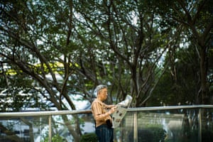 A man reads his newspaper as he stands near trees on an elevated walkway in Hong Kong.