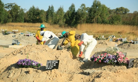 Gravediggers in protective suits fill in a grave amid mounds of other recent burials