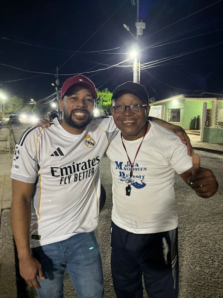 Two men with arms over each other’s shoulders, smiling, with the older one giivng a thumbs up.